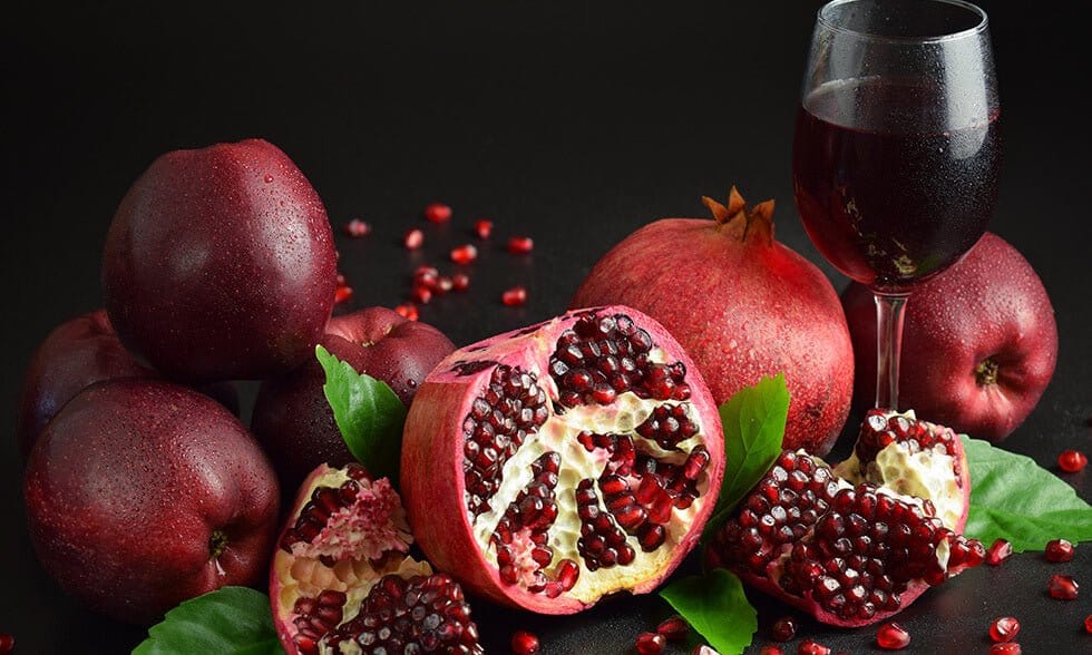 Granateple med røde frukter, delt for å vise saftige frø, sammen med et glass granatepljuice. Mørk bakgrunn.