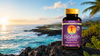 BioAstin Supreme astaxantinflaske med lilla etikett, 60 veganske softgels, stående på steiner med hav og solnedgang bakgrunn.