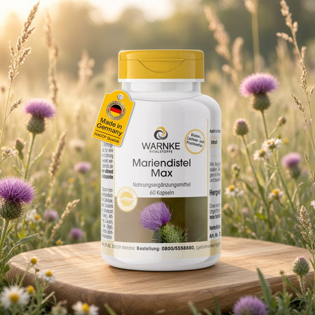 Mariendistel Max beholder med hvit body og gul skrukork, plassert på treflate med lilla blomster i bakgrunnen.