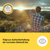 Mann i rutete skjorte sitter på en stein med soloppgang i bakggrunnen, peker utover landskapet.