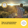 Mann i rutete skjorte som sitter på en stein og ser mot soloppgangen i et fjellandskap.