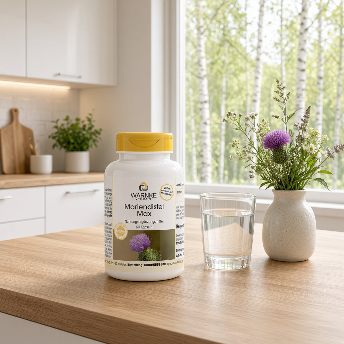 Mariendistel Max-flaske med gult lokk står på et trebord ved siden av et glass med vann og en vase med blomster.