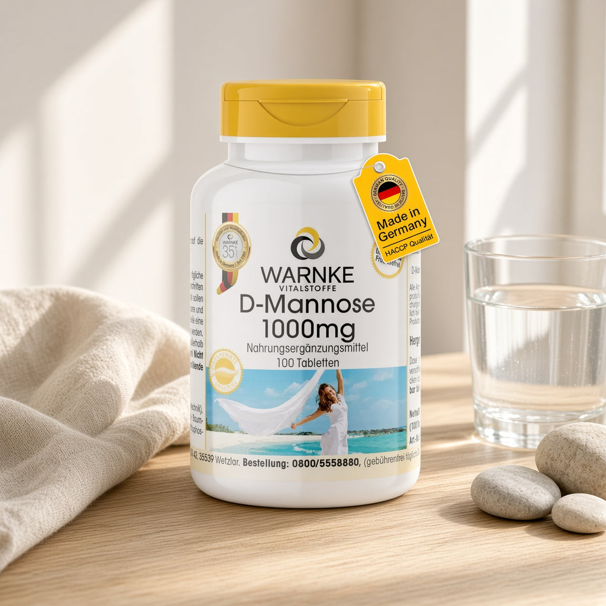 D-Mannose 1000 mg, 100 tabletter i en hvit flaske med gulhet lokk, plassert på et lyst tregulv ved siden av glass med vann.